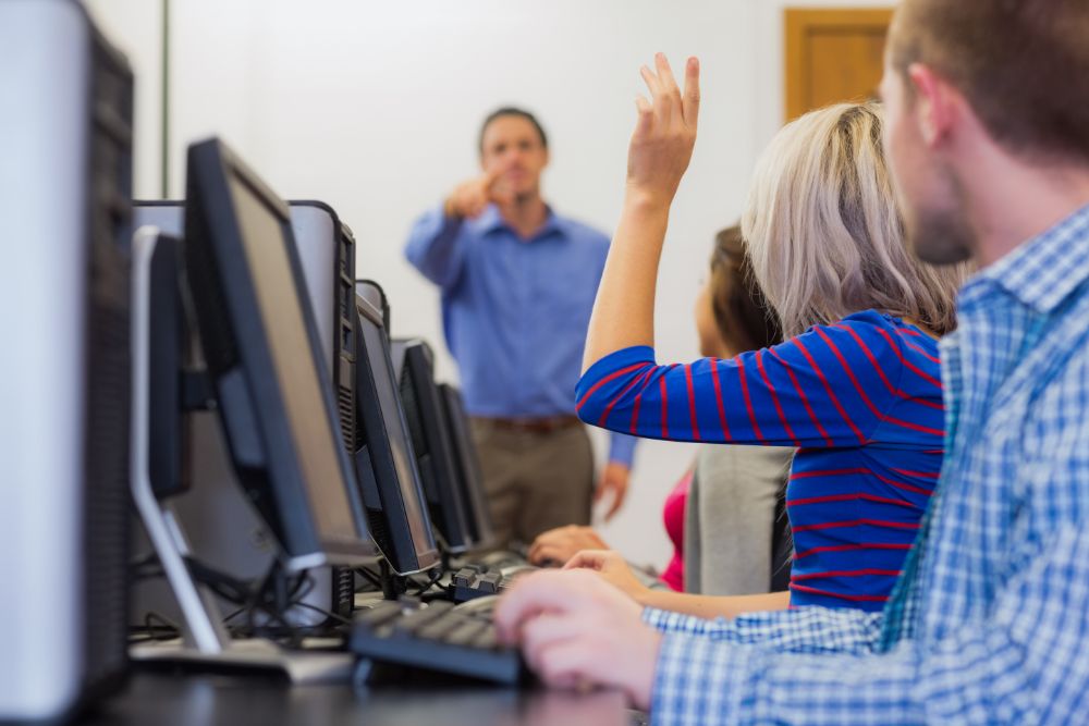 persona delante de ordenadores y una persona  tiene la mano levantada en el curso de ciberseguridad